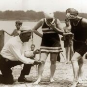 An beach official measures bathing suits to ensure they aren’t too short (1920s)